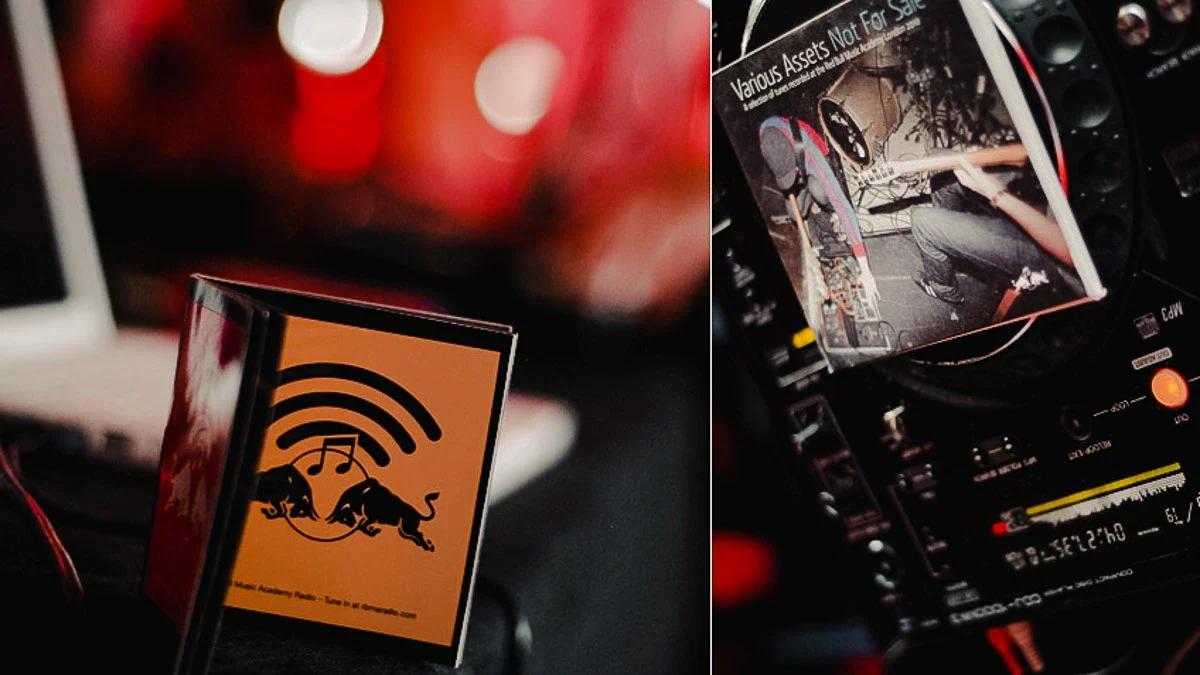 A DJ booth at the Red Bull Music Academy: a Pioneer CDJ deck with a CD sleeve resting on its jog wheel and an Academy Radio booklet standing beside it, lit against red bokeh
